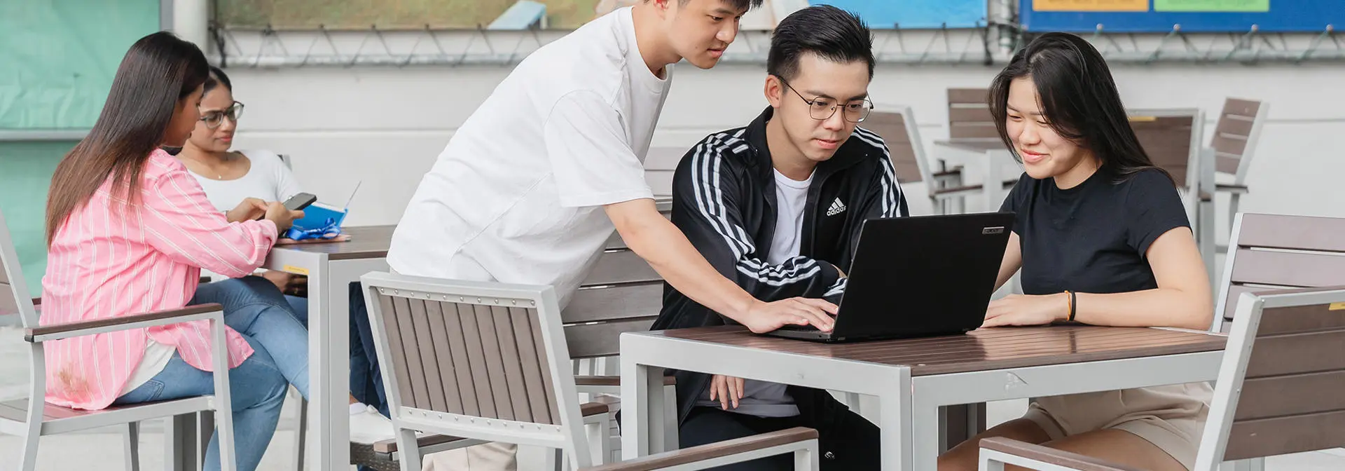 Student sitting outside working on a laptop in a group.