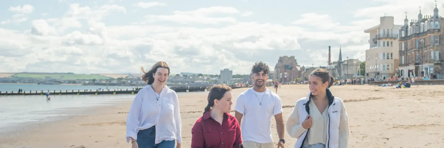 Four individuals walking across a beach with a town in the background.