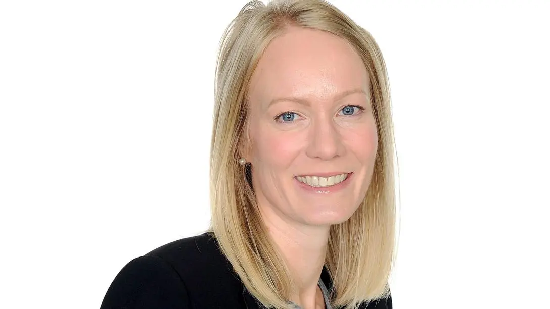 A white woman with medium-length blonde hair smiles in front of a white background