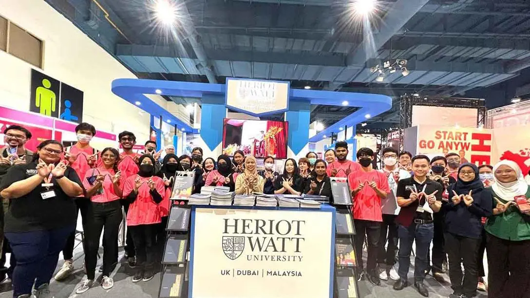 A group of staff and students make a W sign with their hands at the Sureworks Education & Further Studies Fair 2023