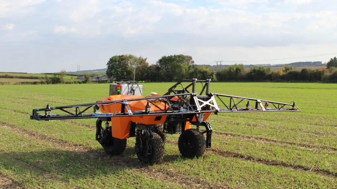 A small orange farming vehicle in a green field under a blur. It has a light metal glider on top that stretches out on either side.