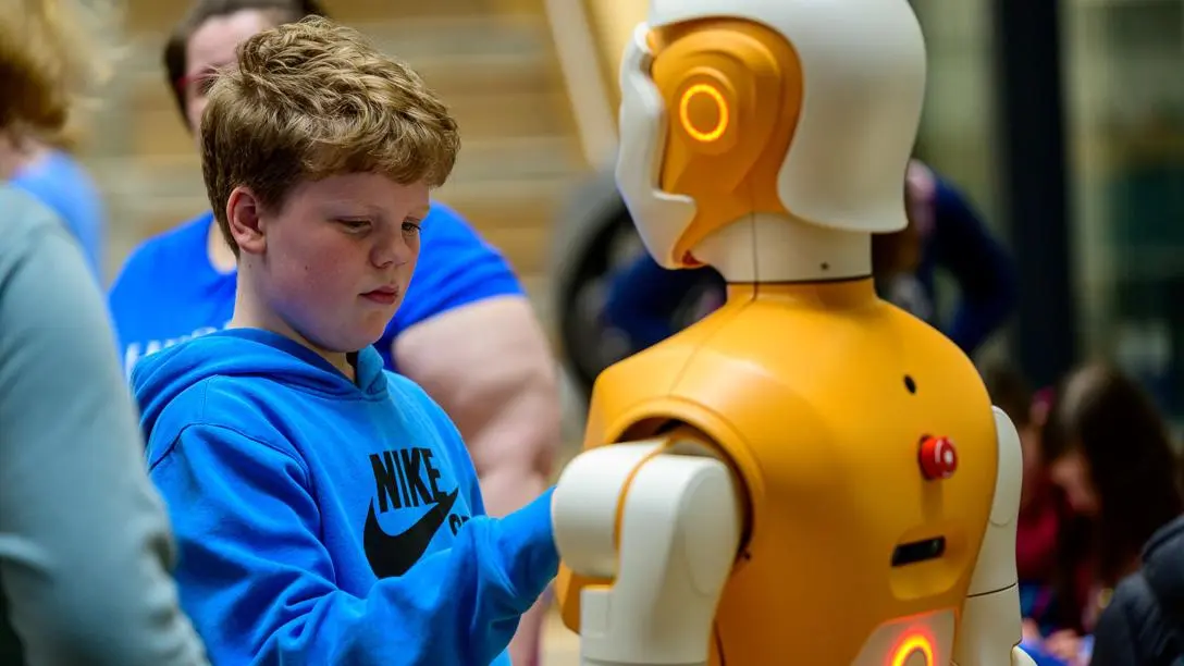 A young man with reddish hair plays with an ARI humanoid robot