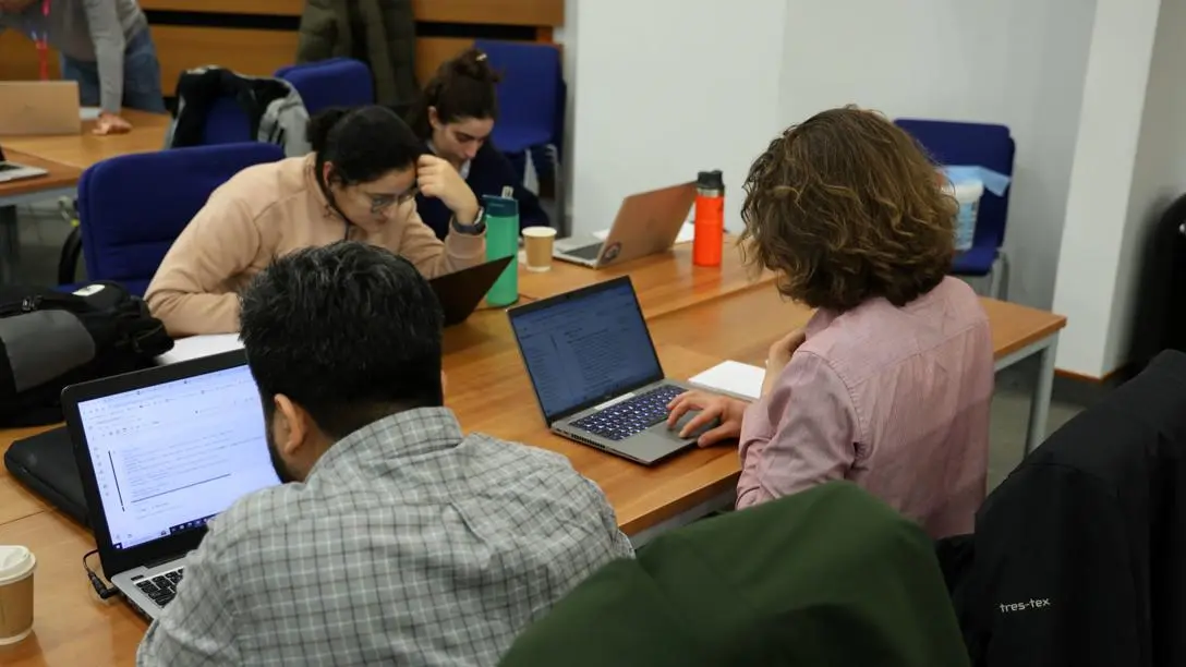 Four students around a desk working on laptops