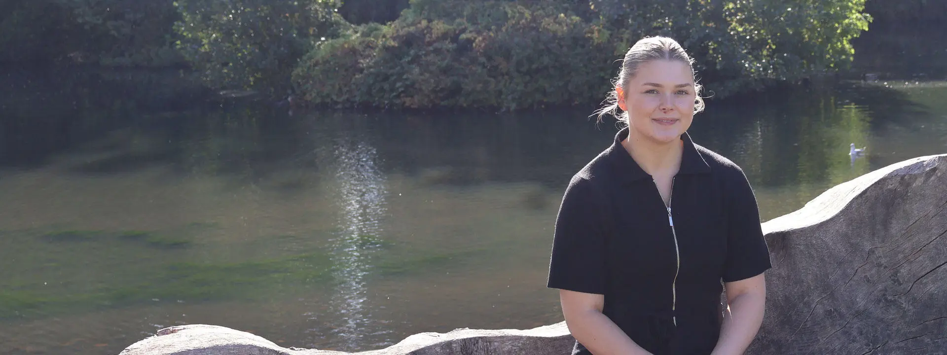 Beth A smiling in the sunshine in front of the Edinburgh Campus loch.