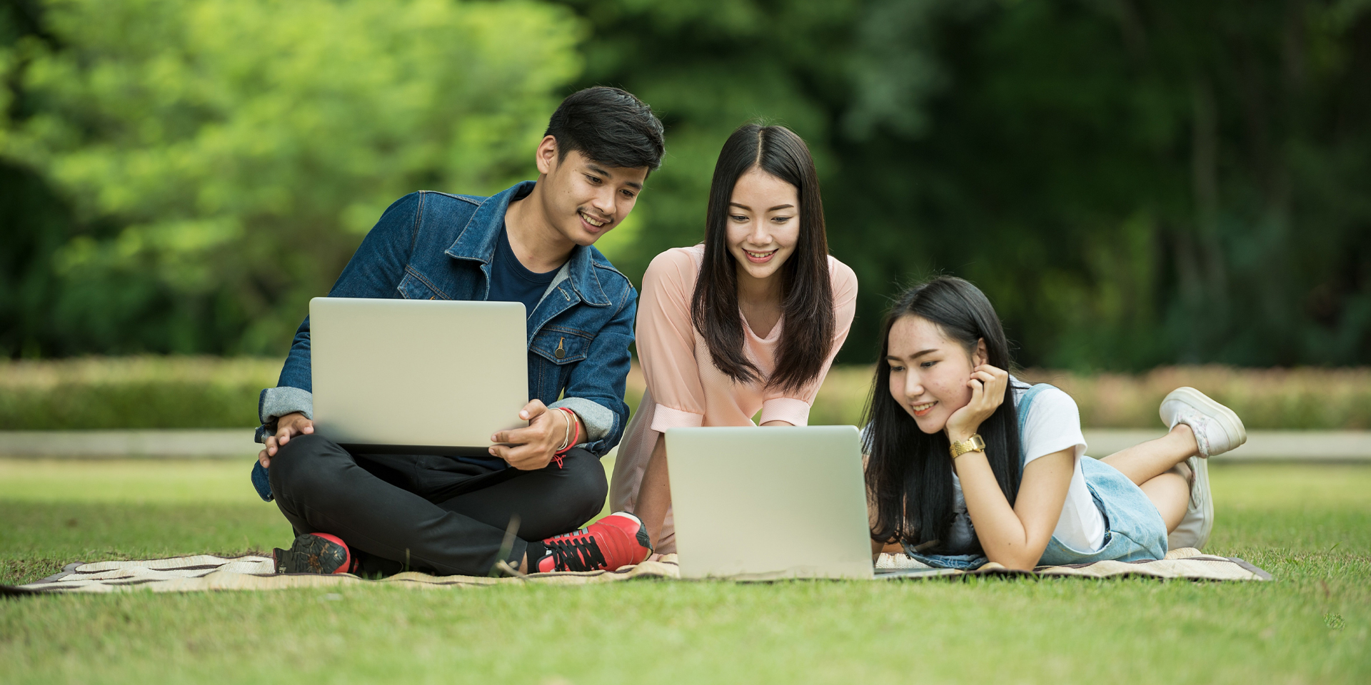 Students using laptops while sitting on a blanket outdoors.