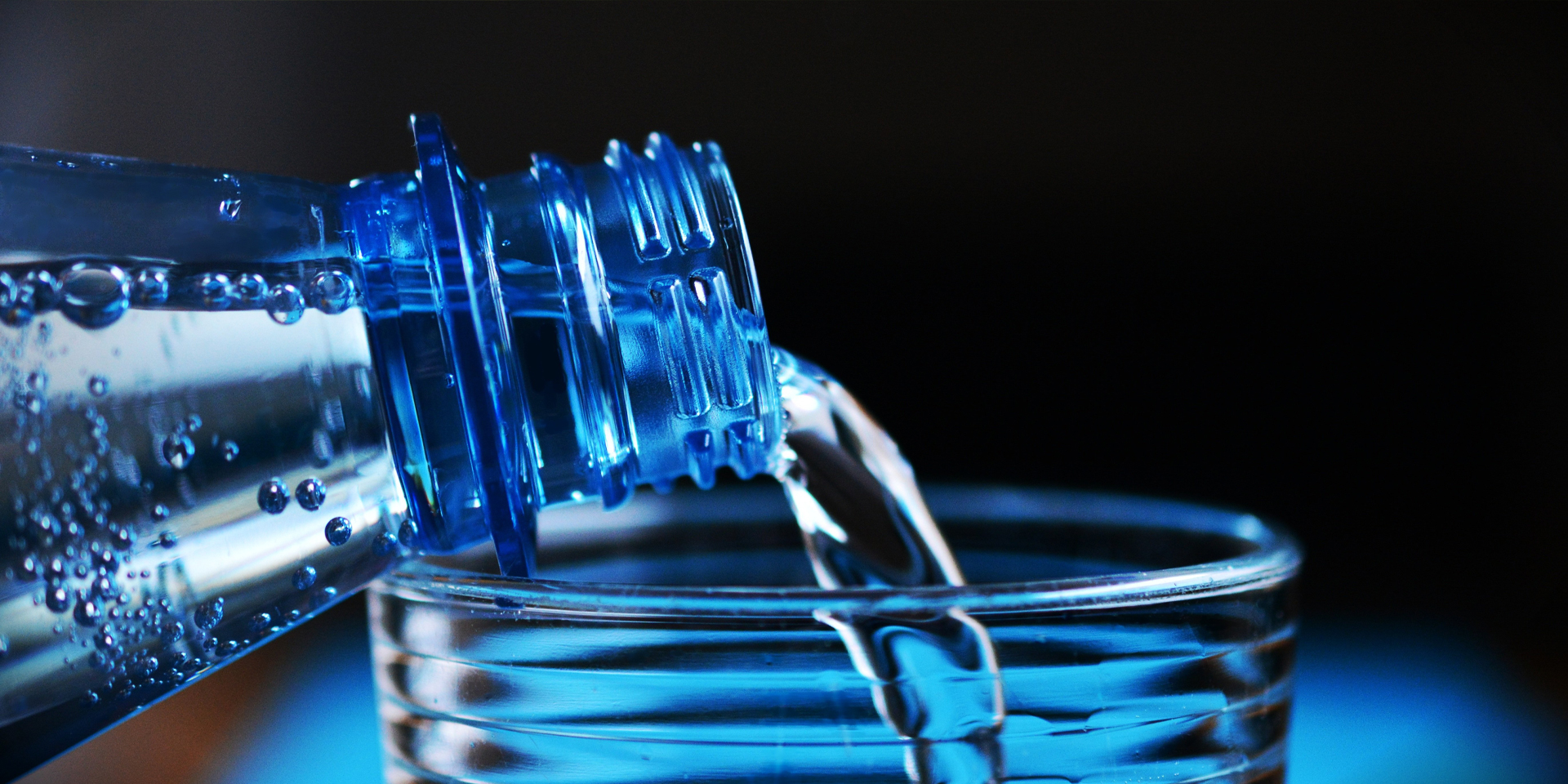 Close-up of sparkling water being poured from a blue plastic bottle into a glass.