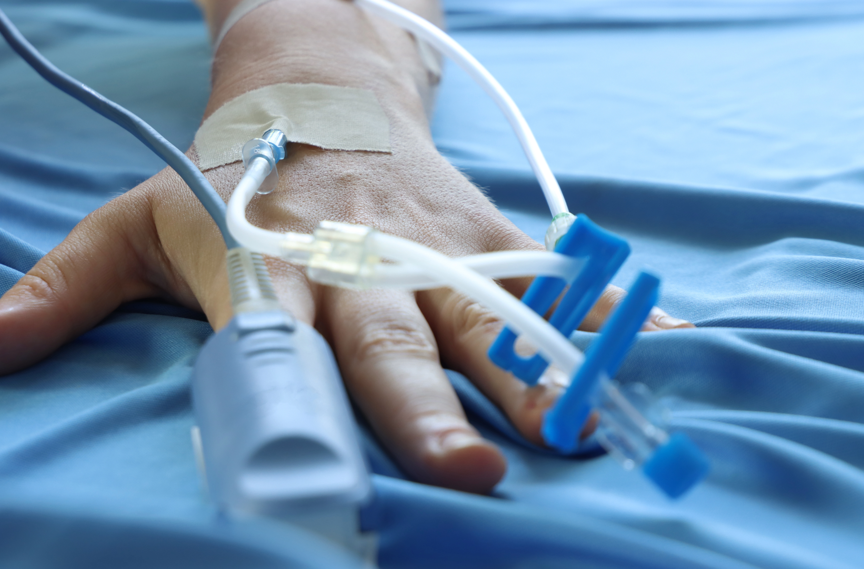 Hand on hospital linens with medical monitoring wires. 