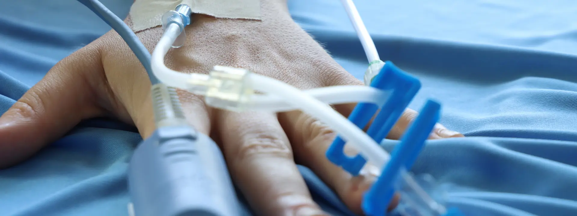 Hand on hospital linens with medical monitoring wires.