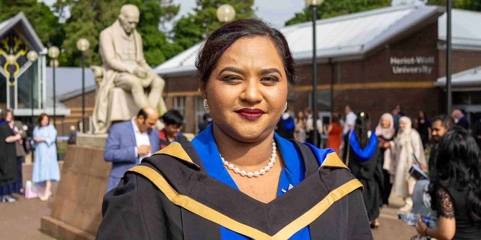Graduate Helan Vinod, standing outside the main entrance of Heriot-Watt University