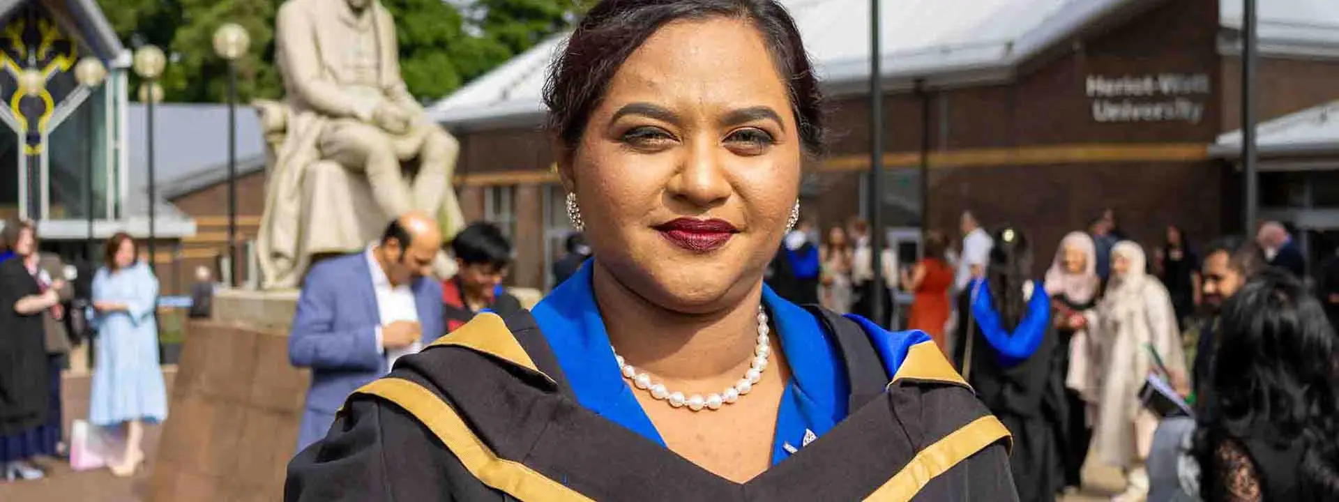 Graduate Helan Vinod, standing outside the main entrance of Heriot-Watt University