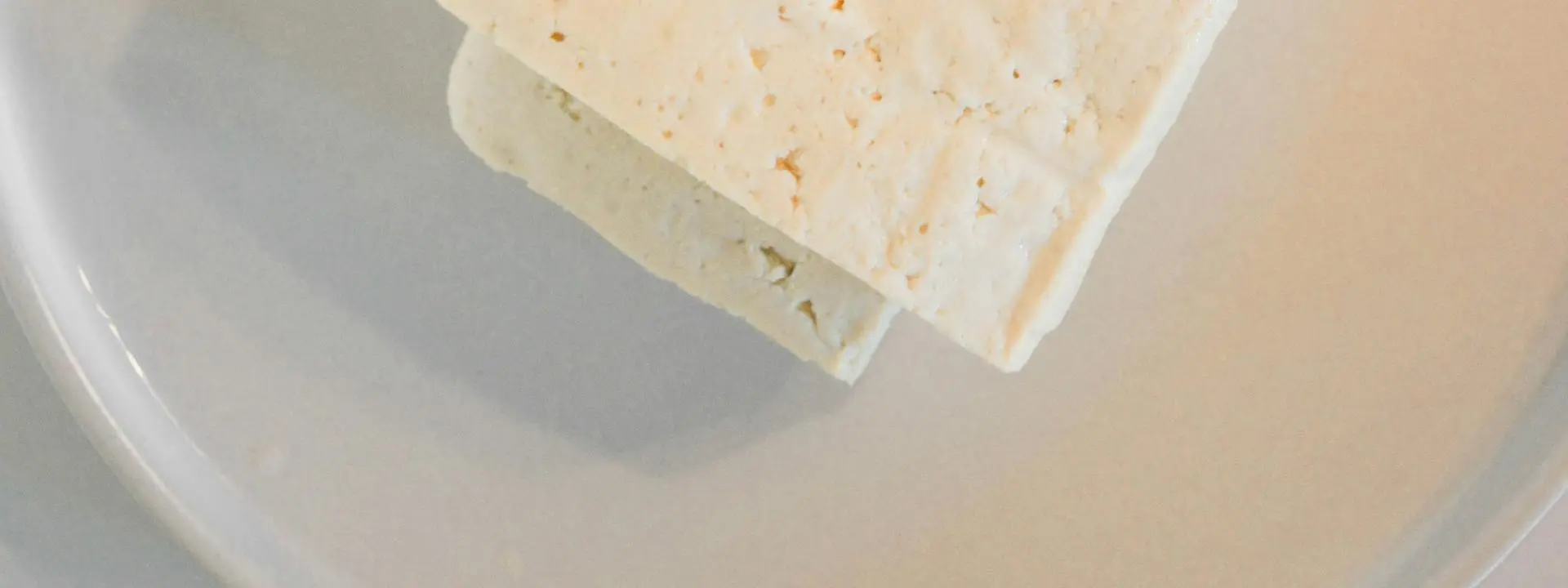 Slice of cheese pictured on a white plate.