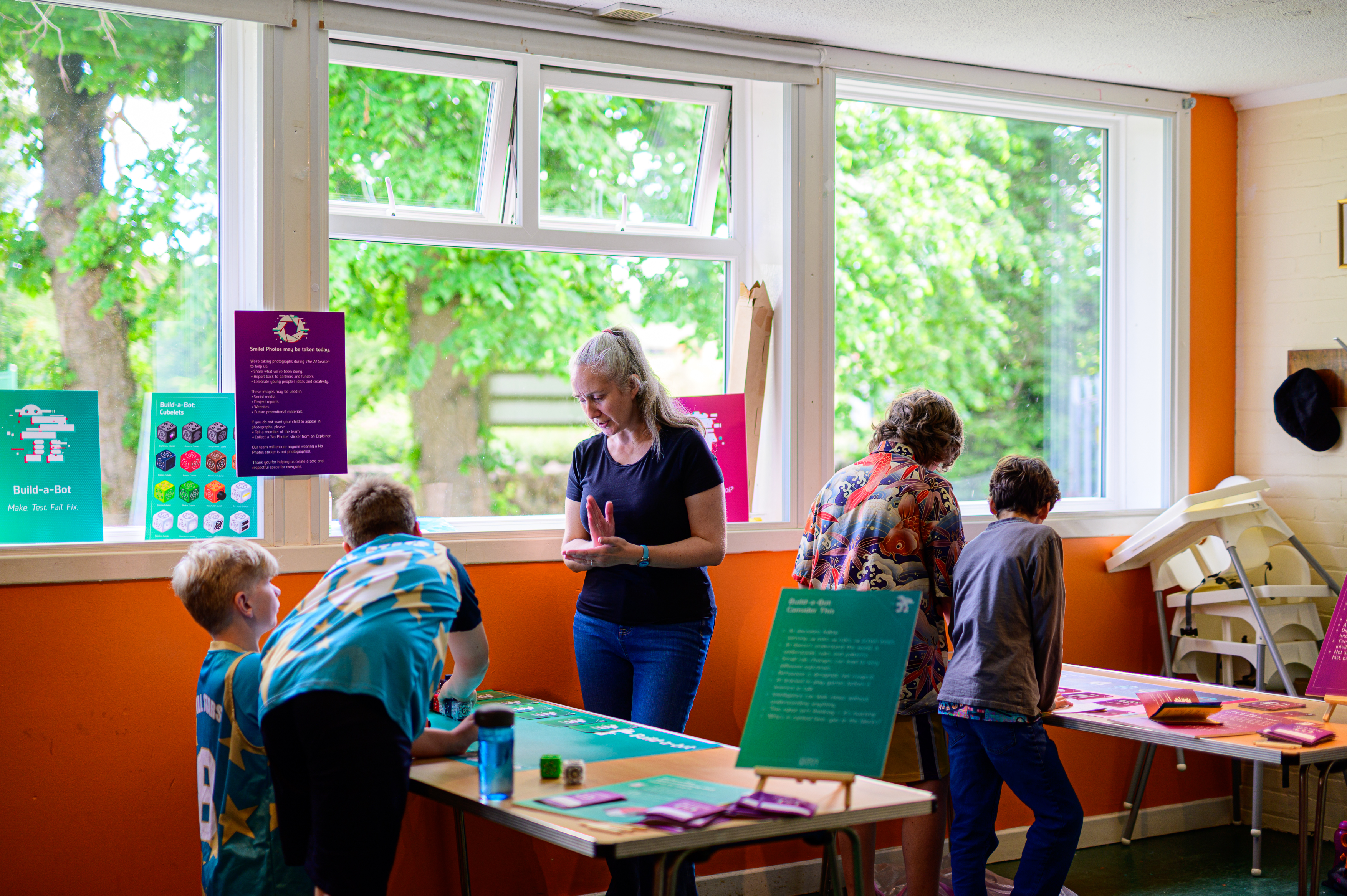 A group of children supervised by adults gathered around the tables with colourful leaflets
