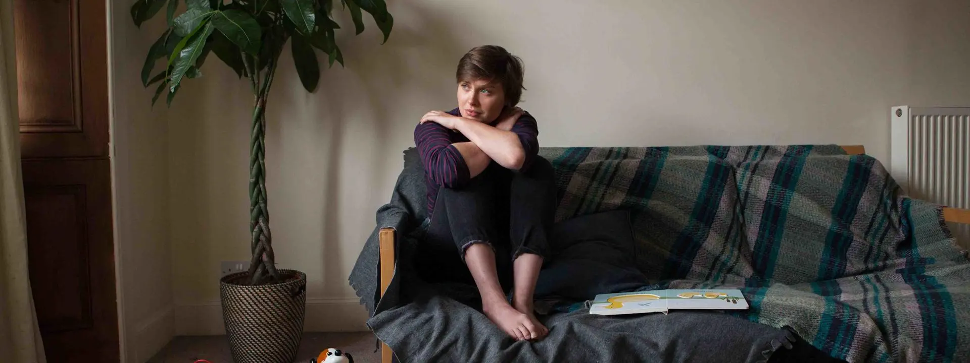 Image shows a woman, looking tense and sitting on a couch in a family setting.