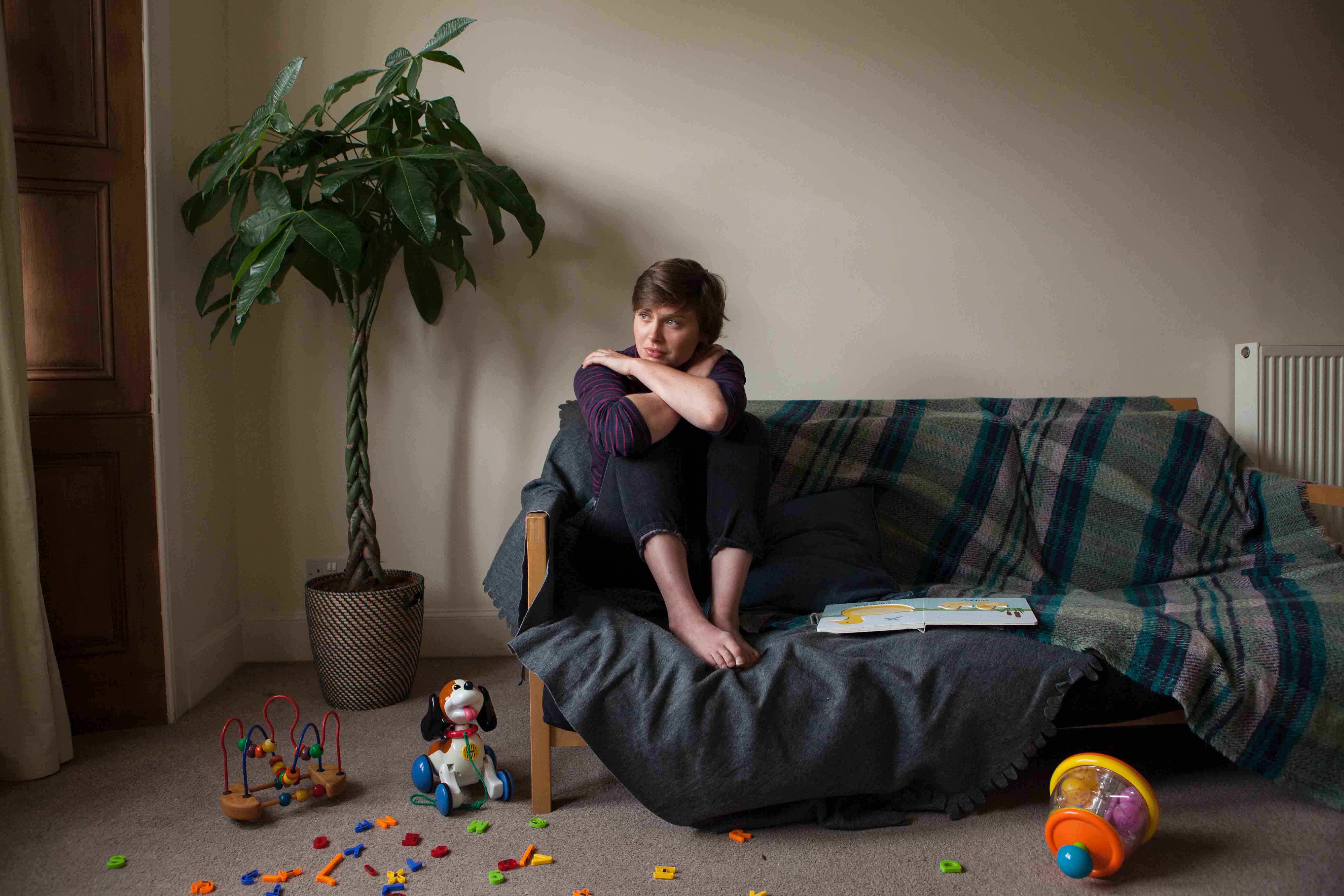 Image shows a woman, looking tense and sitting on a couch in a family setting. 
