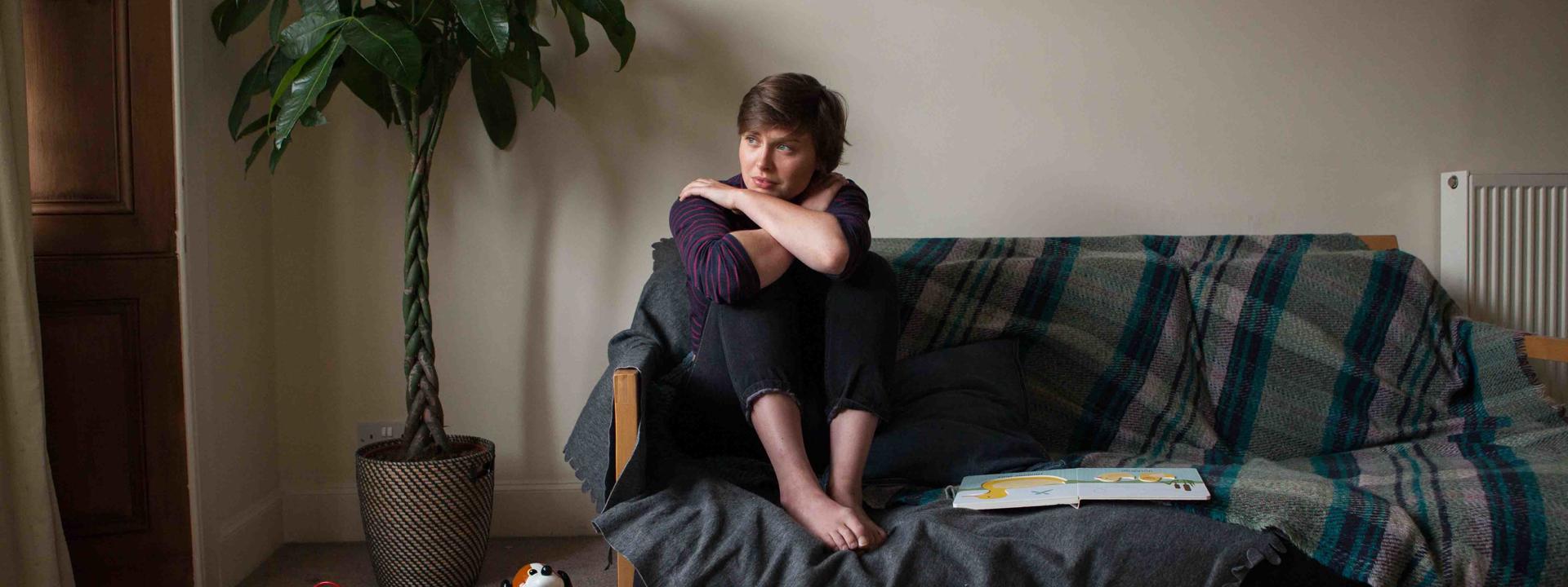 Image shows a woman, looking tense and sitting on a couch in a family setting.