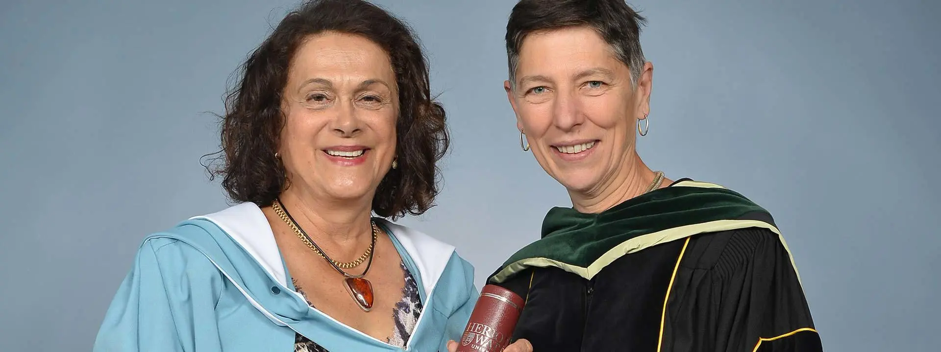 Dr Chehrzad Shakiban (left) and Professor Beatrice Pelloni. Both are wearing graduation gowns, facing forward