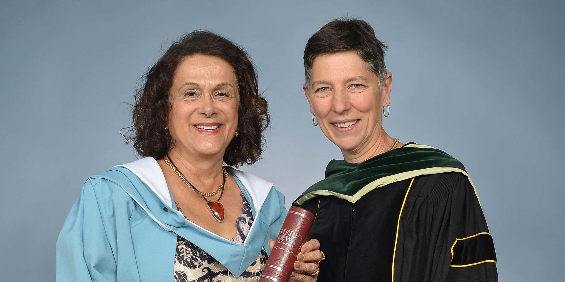 Dr Chehrzad Shakiban (left) and Professor Beatrice Pelloni. Both are wearing graduation gowns, facing forward