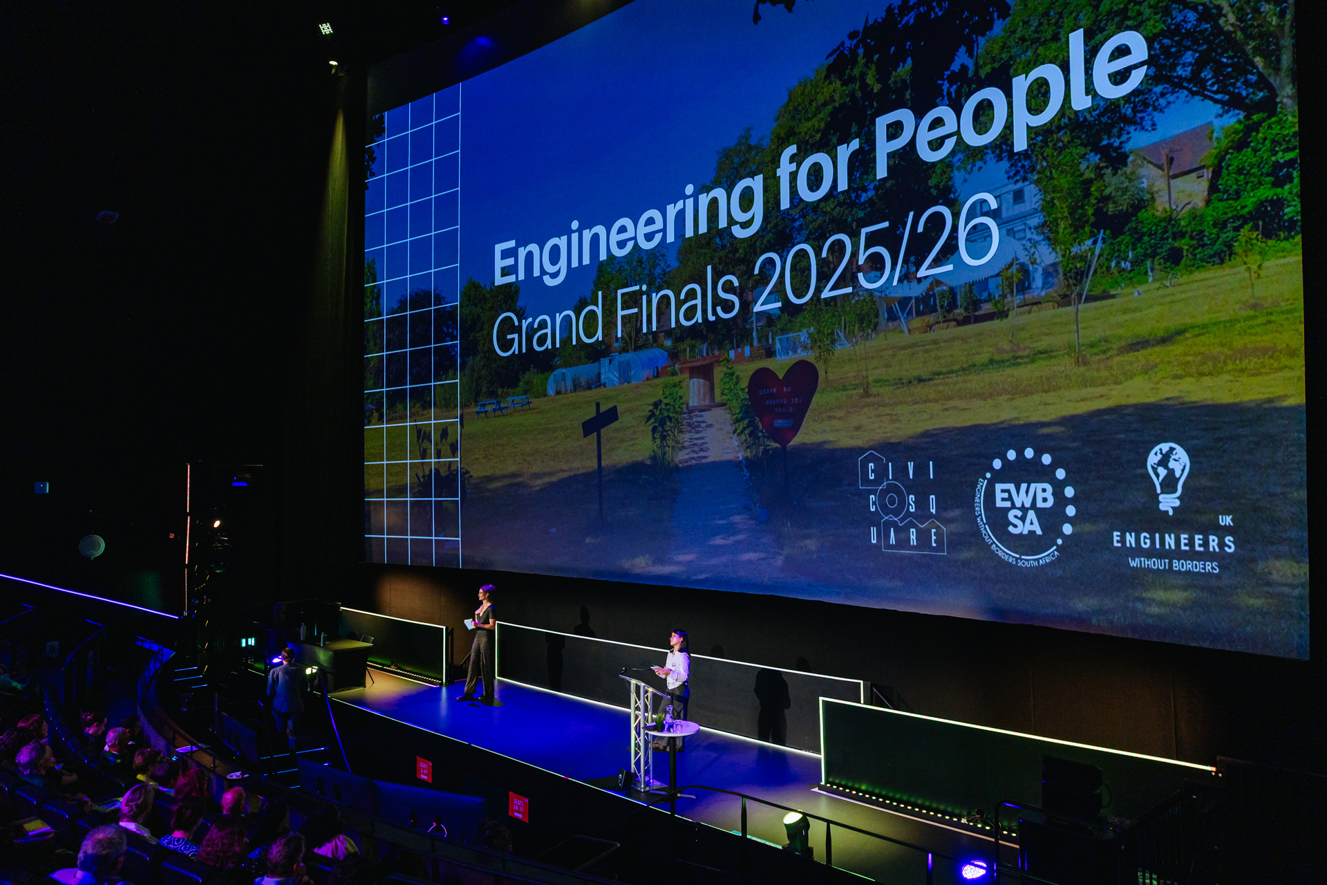 Students presenting on stage with the words "Engineering for People Grand Finals 2025/26" written on screen
