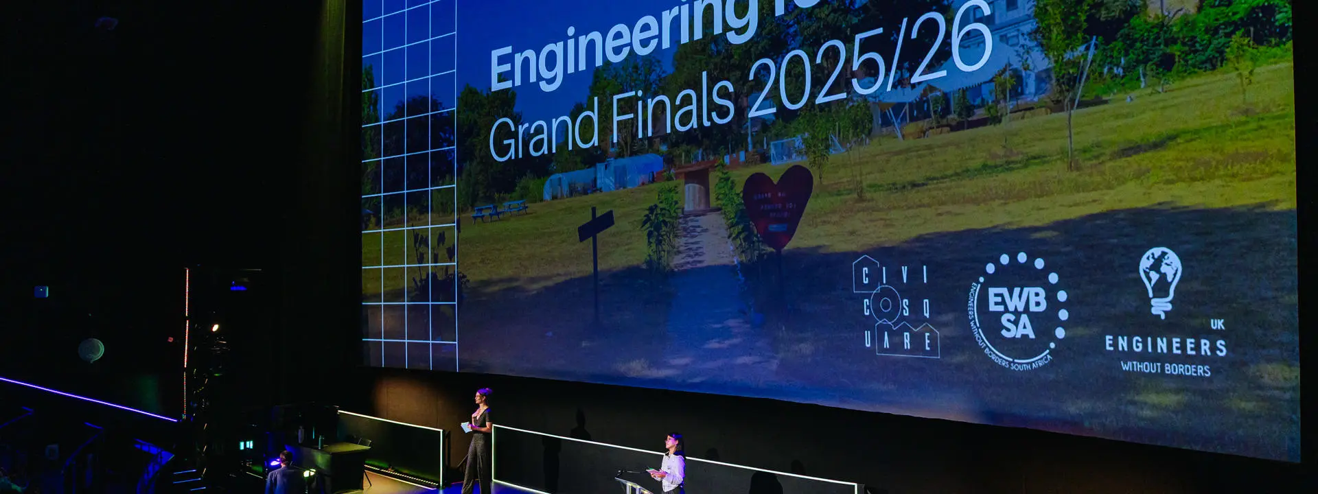 Students presenting on stage with the words "Engineering for People Grand Finals 2025/26" written on screen