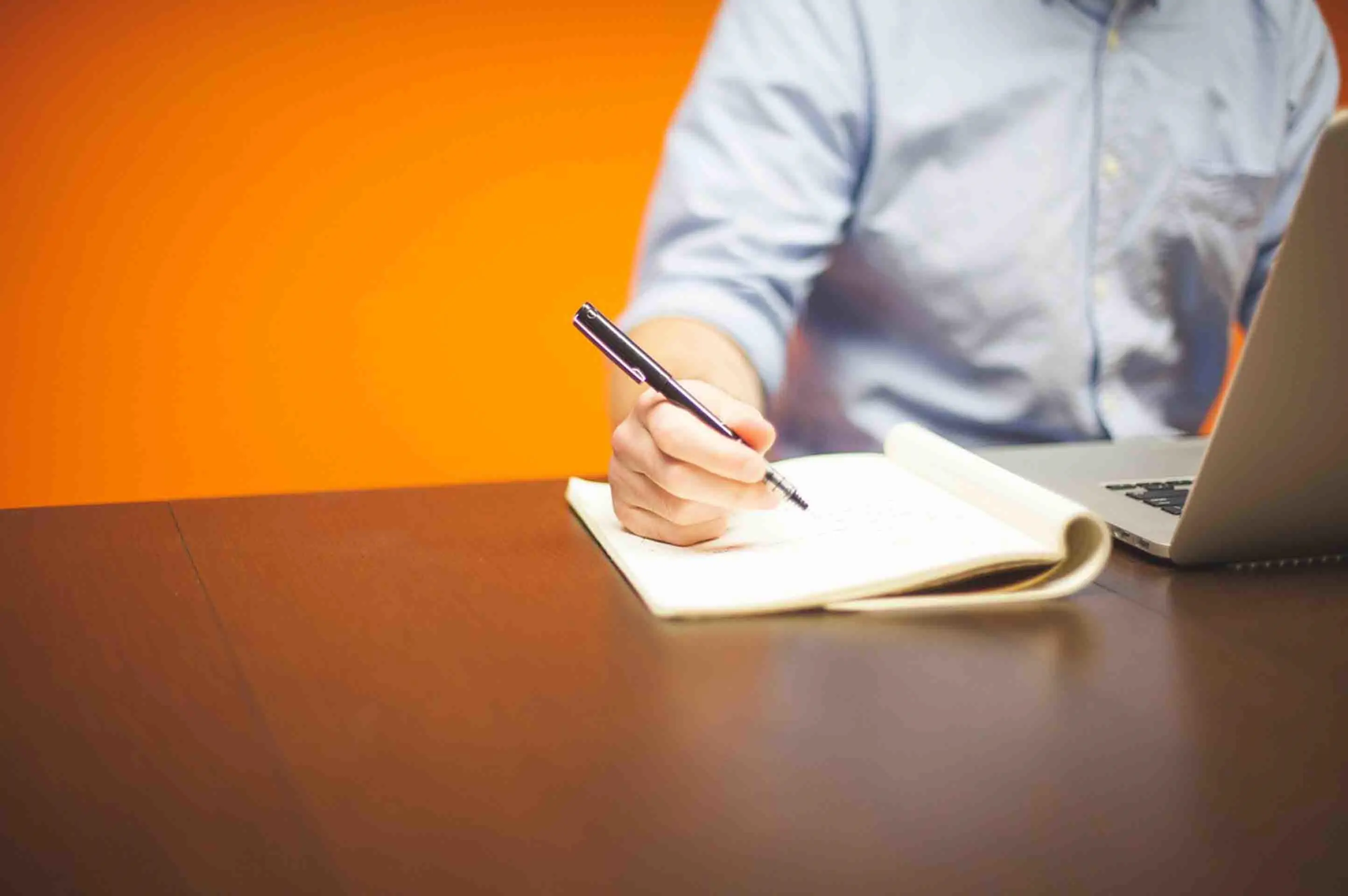 Man sitting in front of laptop, taking notes. 