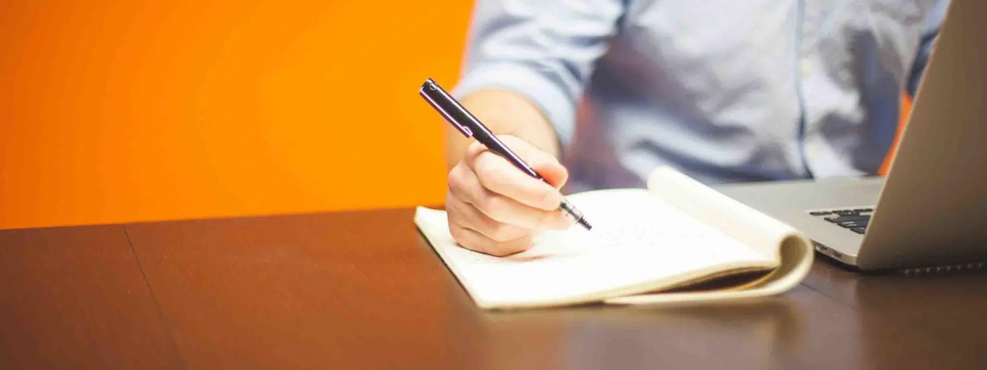 Man sitting in front of laptop, taking notes.