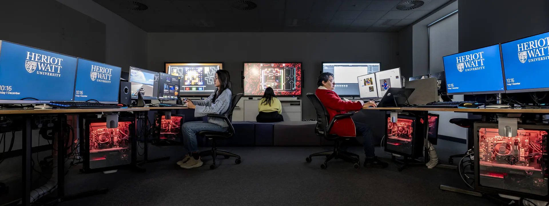 Image shows three people sitting at computer stations.
