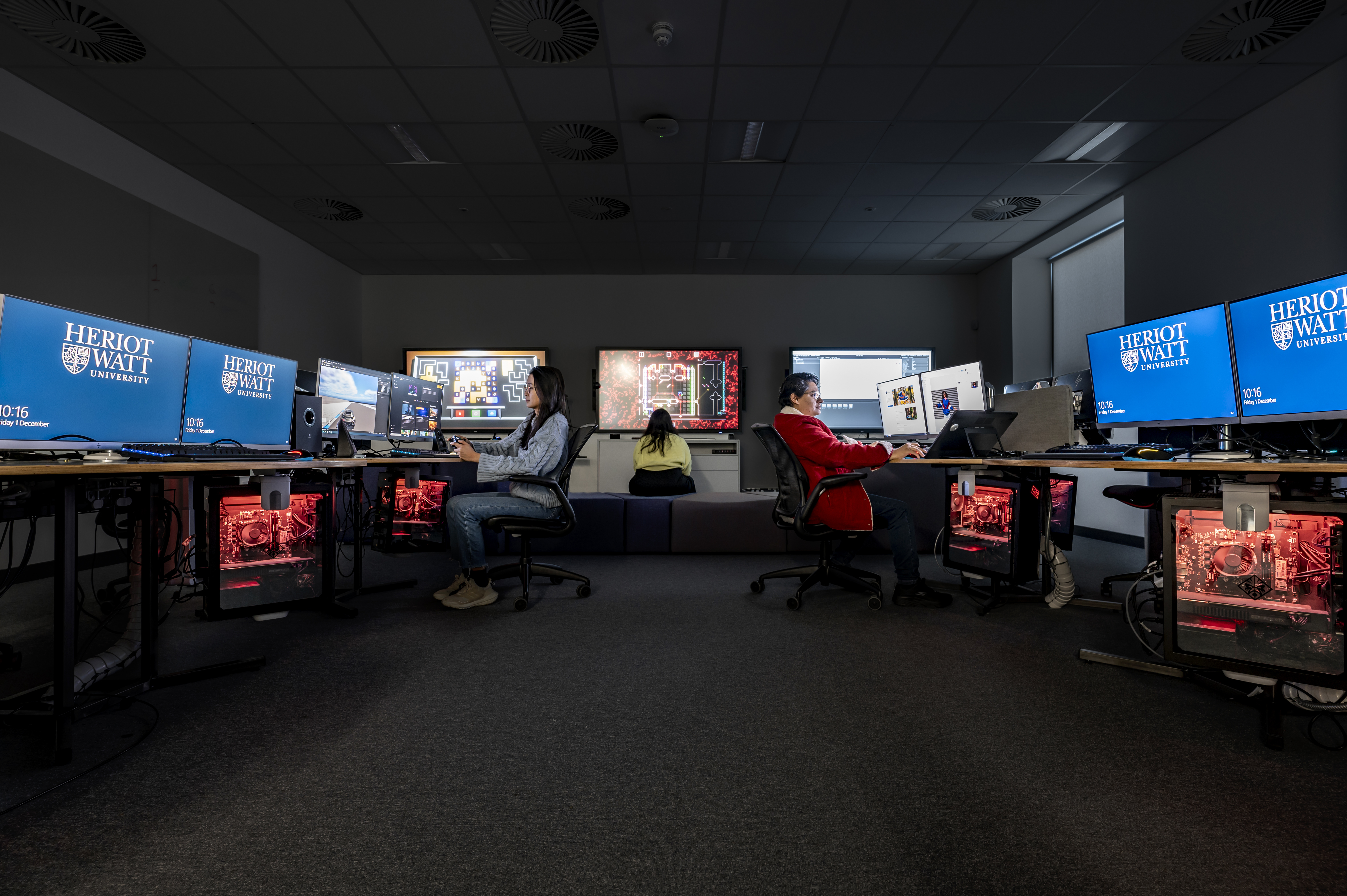 Image shows three people sitting at computer stations. 