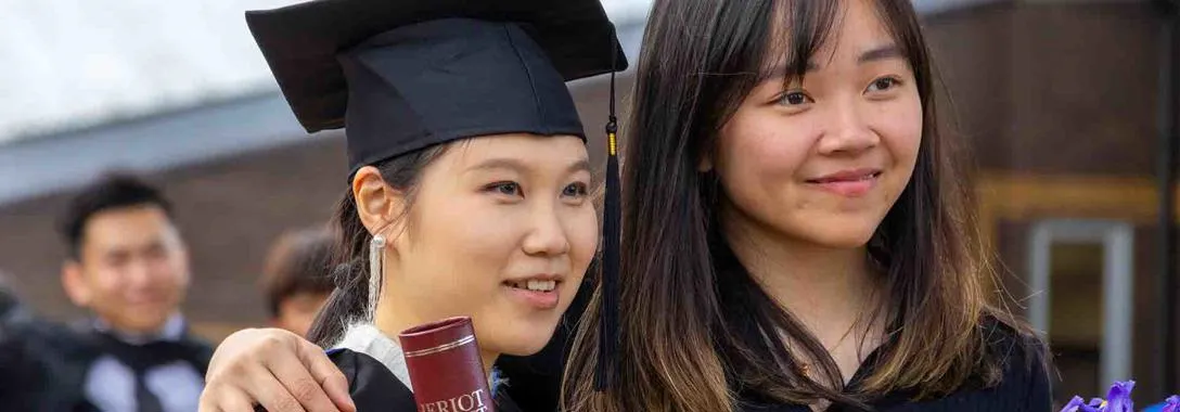 Two students in full graduation dress, pose for a picture at Heriot-Watt University.