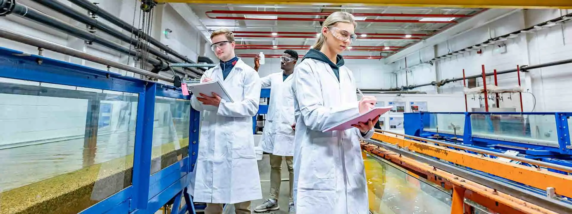 Image shows three students in lab coats, carrying out research.