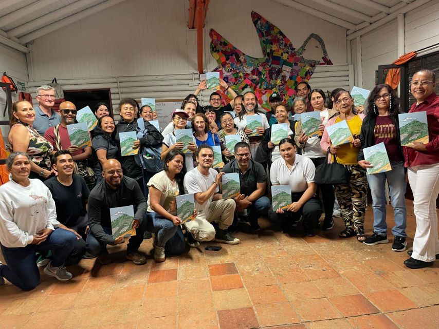 A group of people standing on a tiled floor with a artistic design of a bird behind then, all holding pamphlets of the integrated plan. 