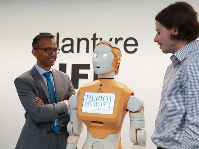 Two individuals standing either side of a humanoid robot named PAL.