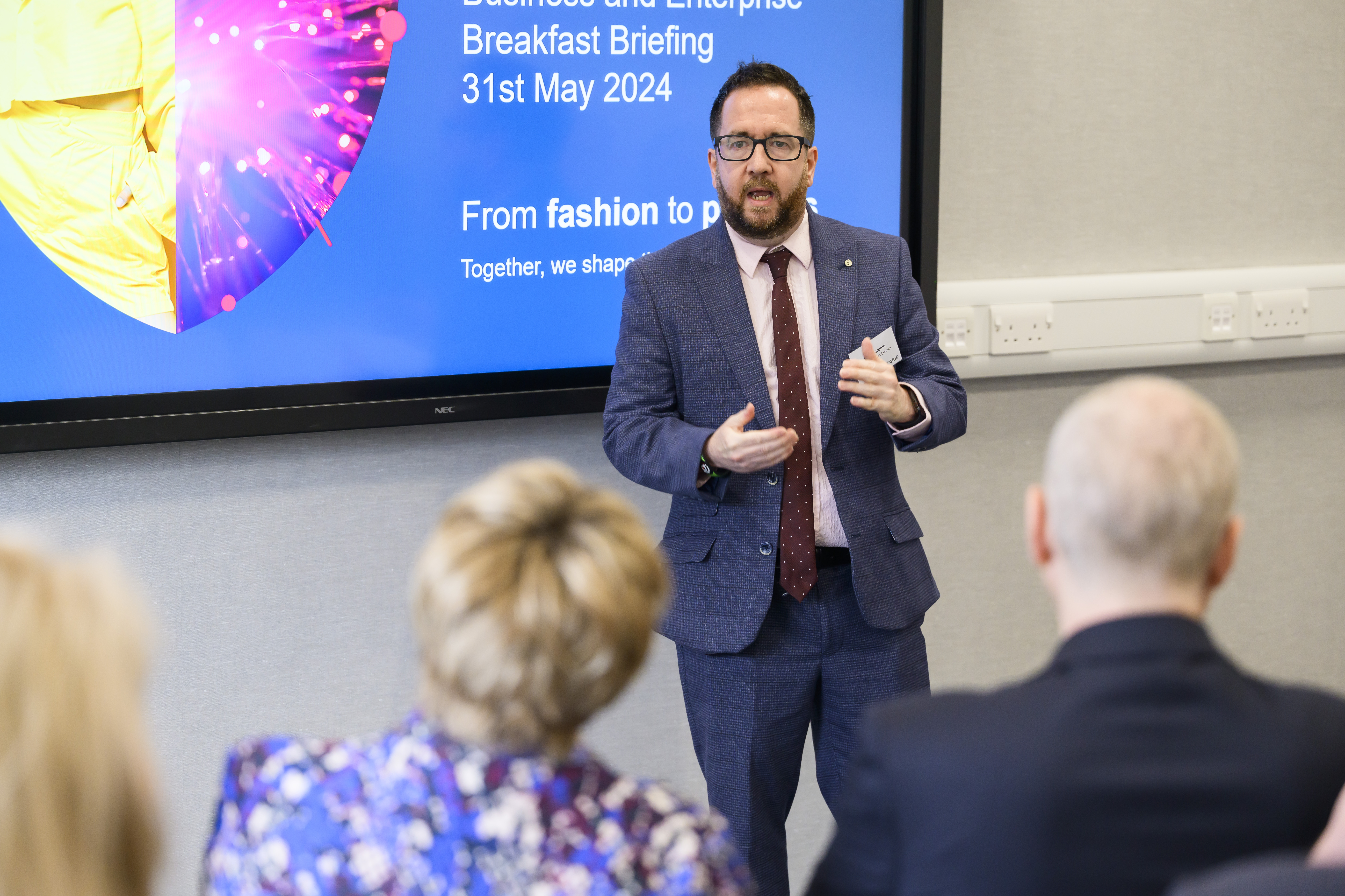 A person presenting on front of a screen that says 'From Fashion to Photons'.