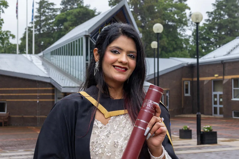 Jaanvi Joshi with her degree outside the Heriot-Watt University main enterance
