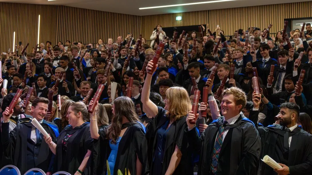 Graduates raise their degree scrolls in a graduation ceremony at Heriot-Watt University.