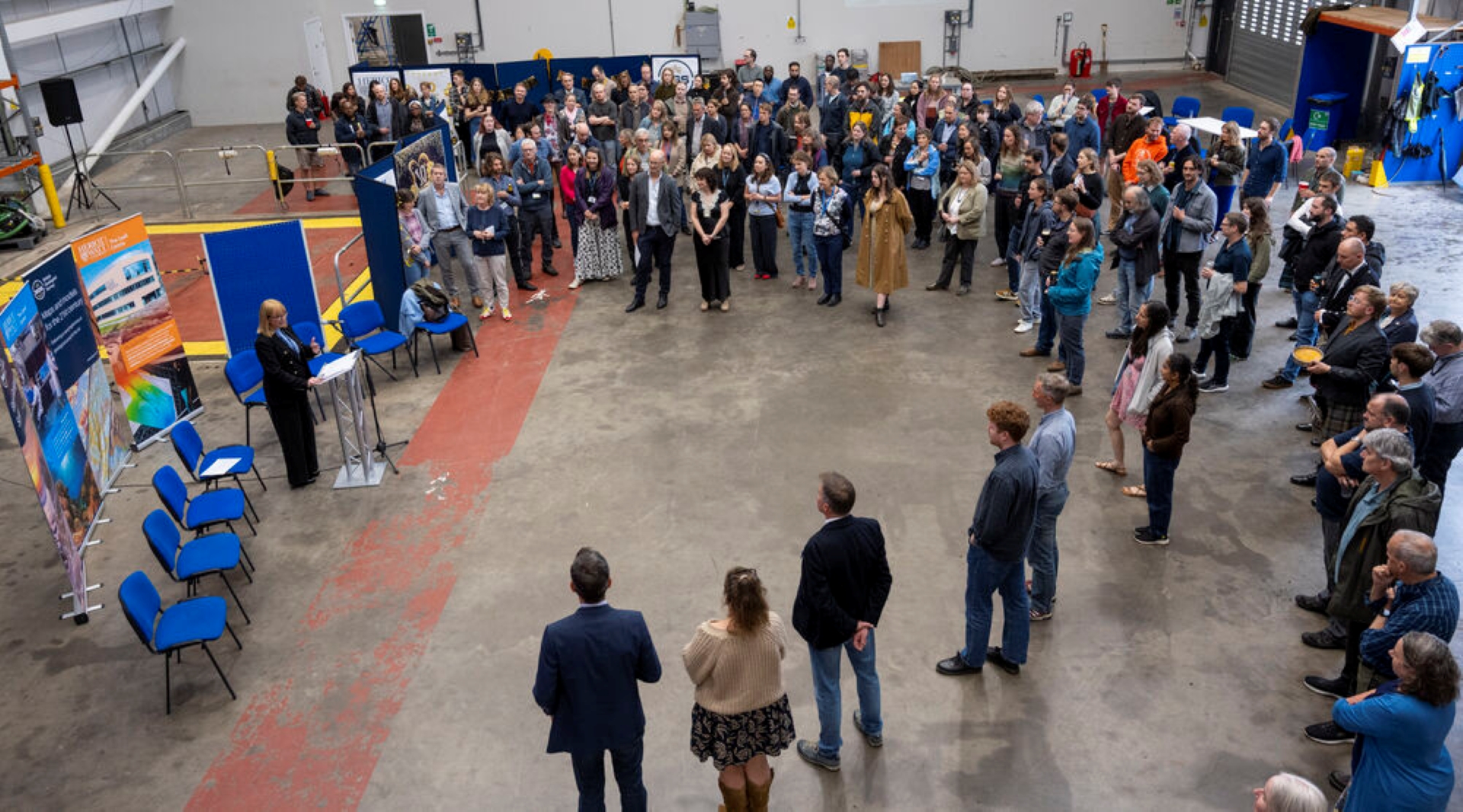 A group of people gathers round as a speech is given.