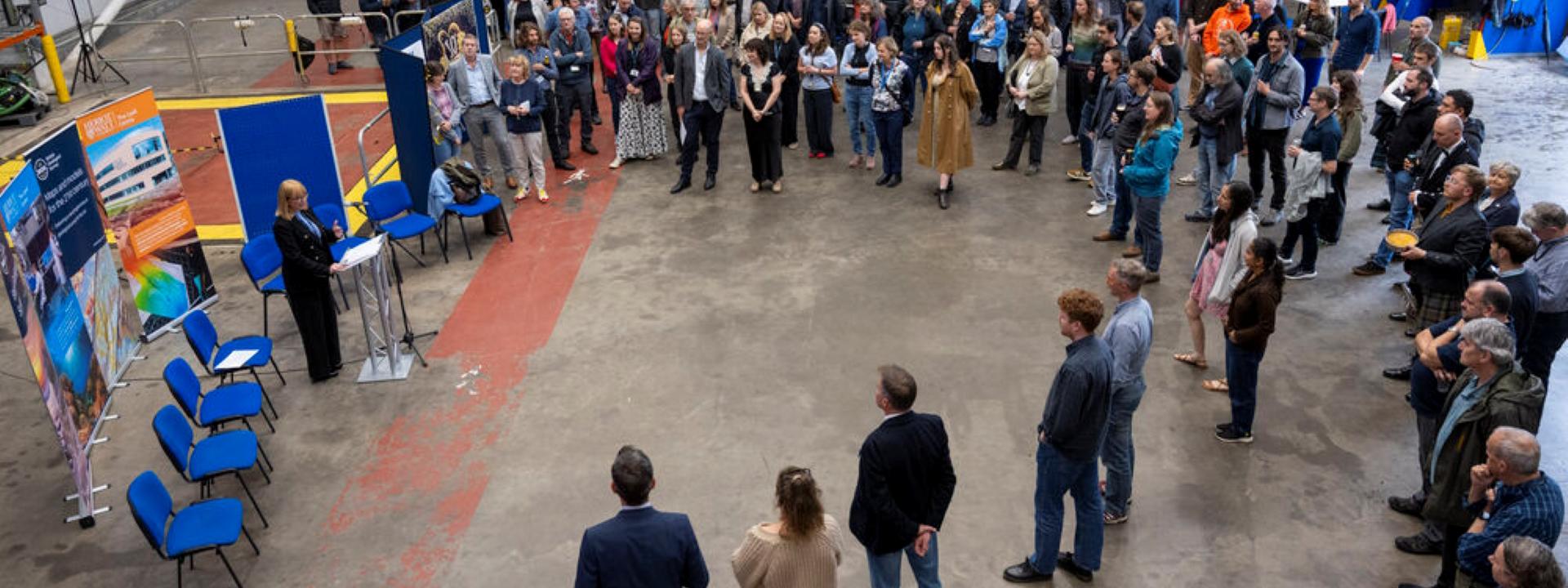A group of people gathers round as a speech is given.