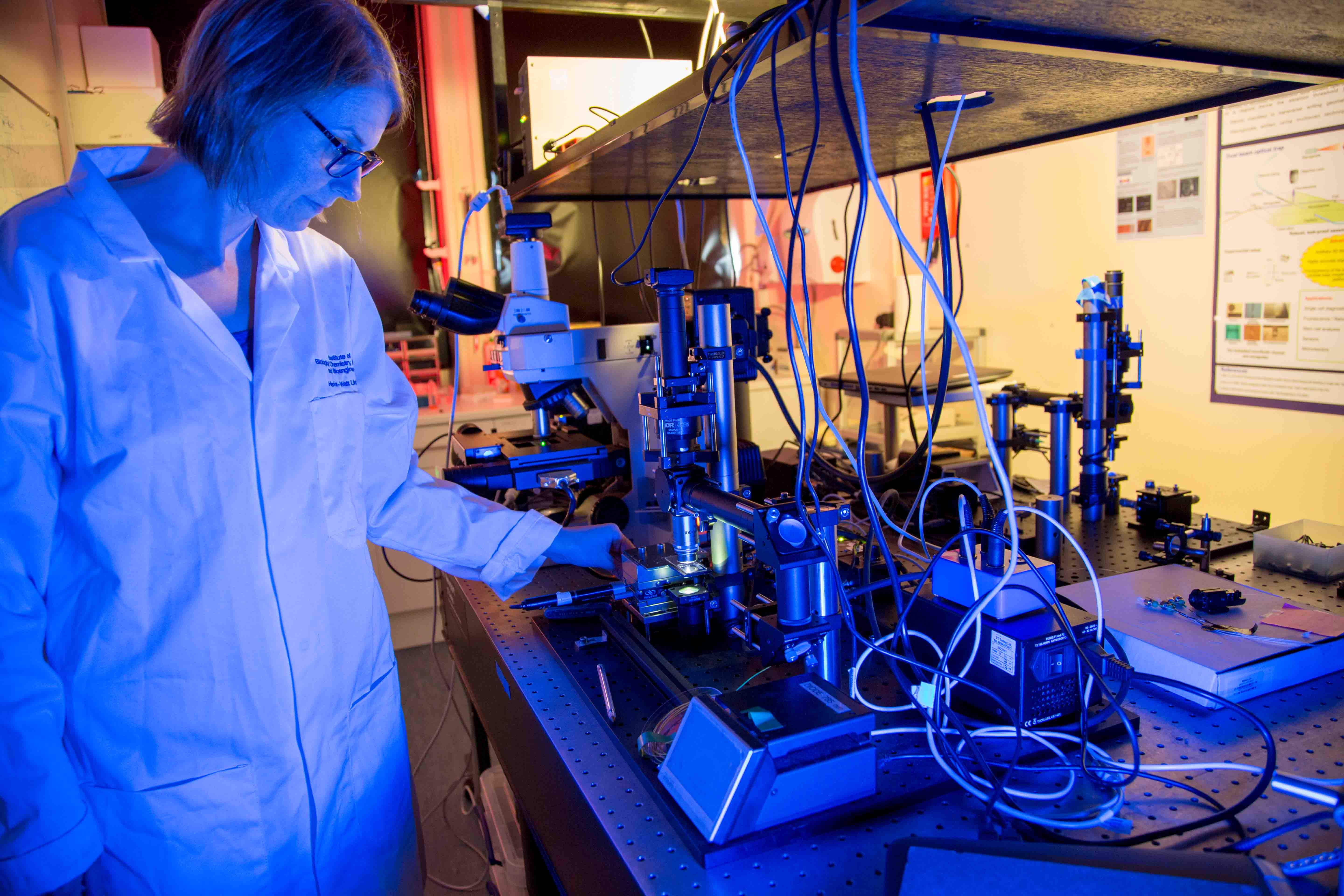 Assistant Professor, Lynn Paterson from u-Care, stands in a lab coat using a microscope. 