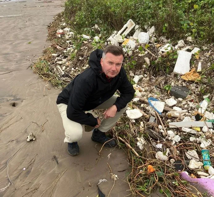 Professor Michel Kaiser (pictured here in Vietnam) led the study alongside Dr Ngo Thi Thuy Huong at Phenikaa University. A person crouches on a sandy beach beside a large accumulation of plastic foam, bottles, sticks,