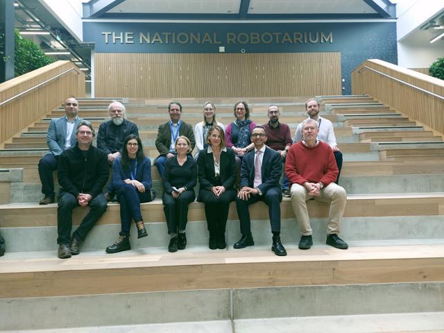 A group of people in business attire are sat across a large stairway at The National Robotarium