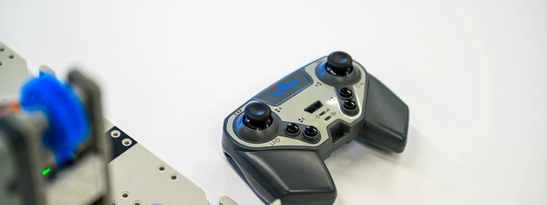 A handheld VEX robotics controller rests on a white tabletop