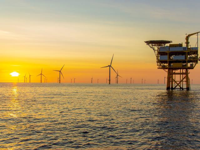 The image shows an ocean scene at sunset with an offshore wind farm.