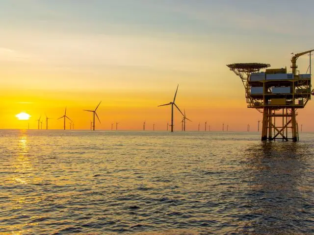 The image shows an ocean scene at sunset with an offshore wind farm.