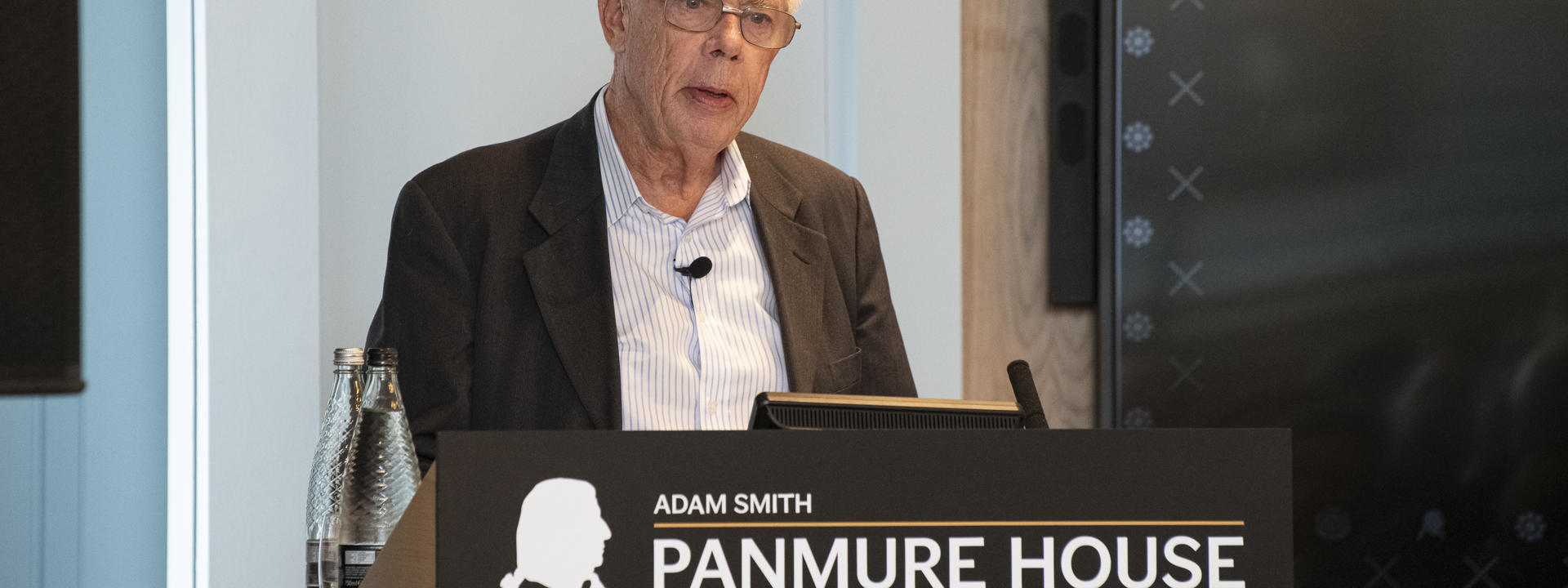 Professor Sir John Kay standing at a lectern.