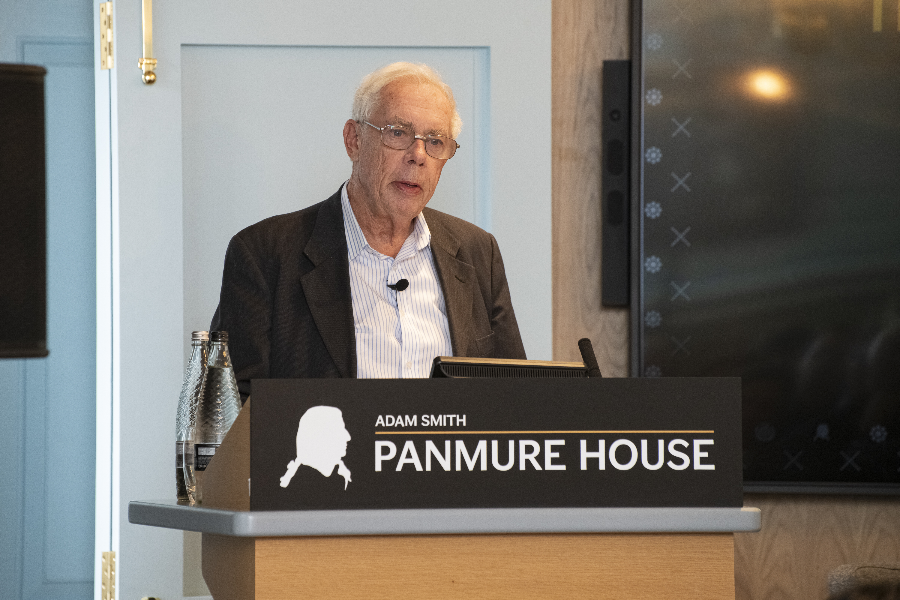 Professor Sir John Kay standing at a lectern. 