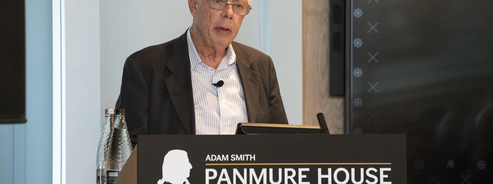 Professor Sir John Kay standing at a lectern.
