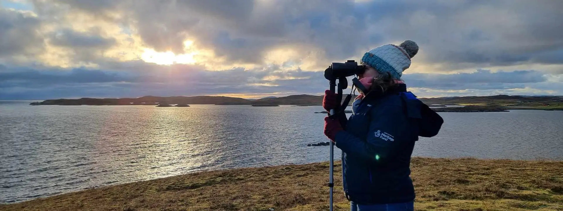 Image shows a researcher, using binoculars to look out to sea.