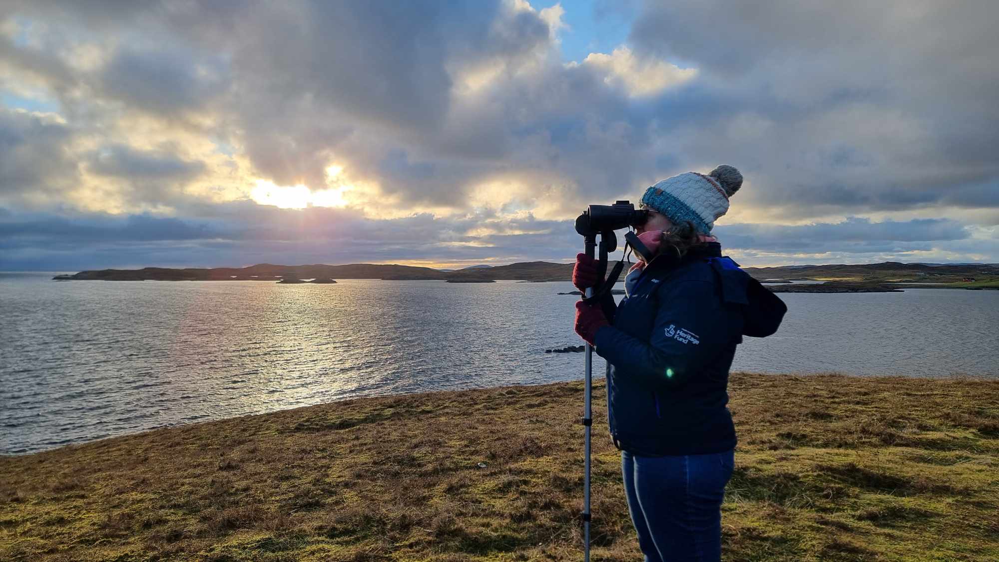 Image shows a researcher, using binoculars to look out to sea. 
