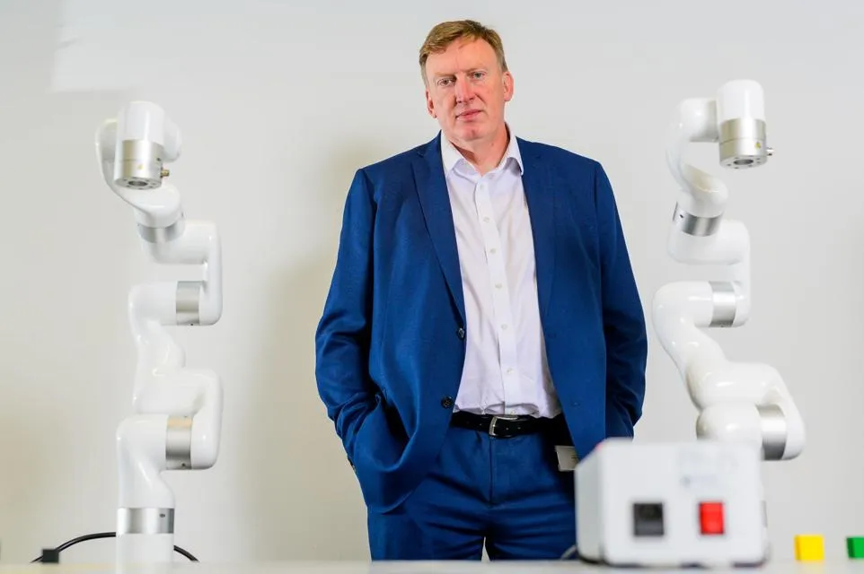 A man in a blue suit standing between two robotic arms