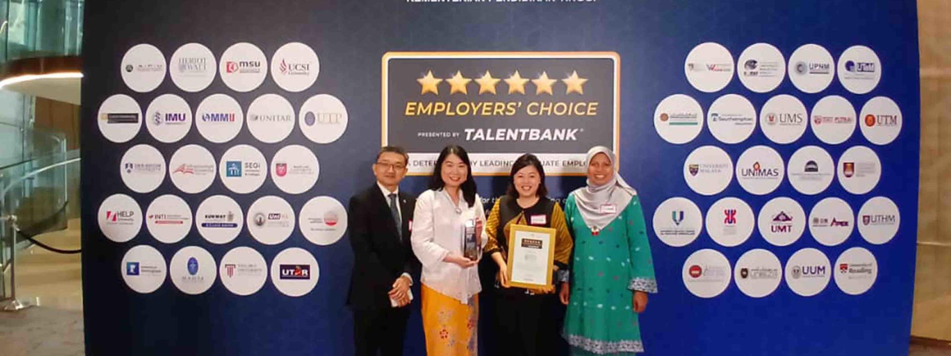 Image shows four people standing in front of a large banner with once holding a framed certificate.