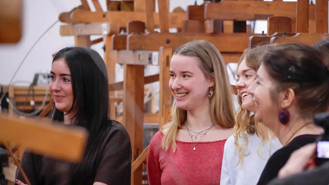 Group of three students and teacher smiling with looms in background 